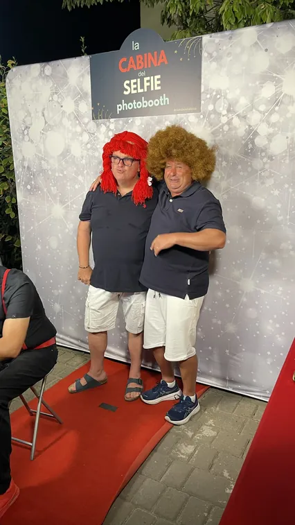 Ospiti travestiti con parrucche e cappelli davanti al fondale, Ferragosto 2026